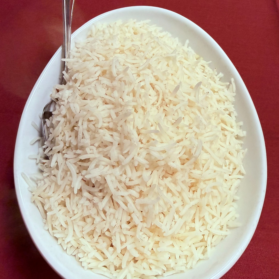 White bowl filled with fluffy long-grain rice and a metal spoon on a red tablecloth.