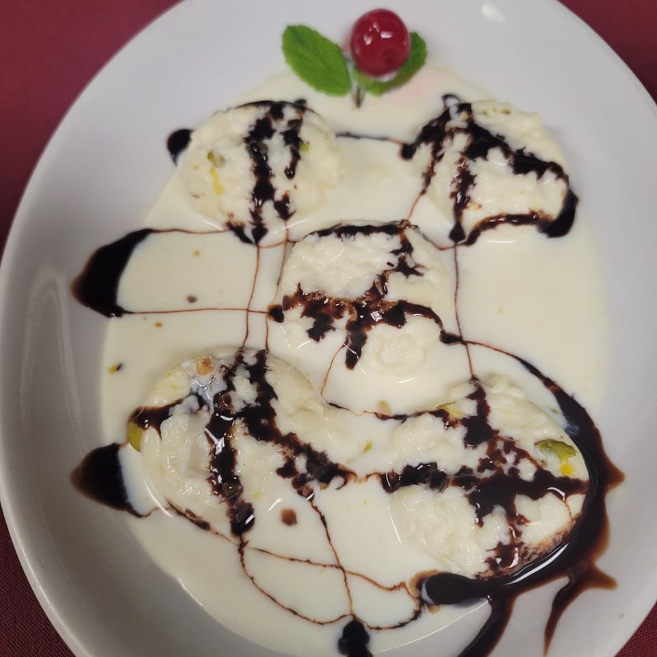 Indian dessert with four white patties drizzled with chocolate sauce, a cherry, and mint.