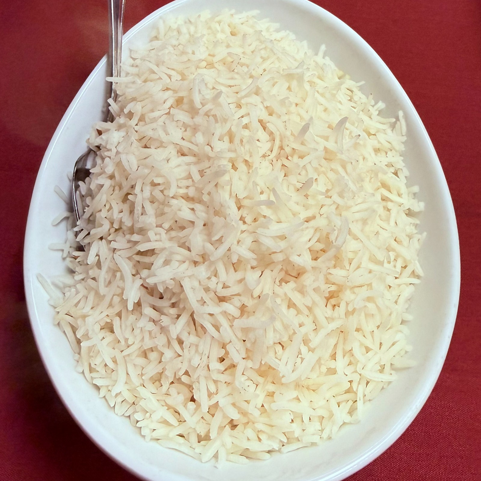 White oval plate filled with steamed long-grain rice on a red tablecloth, with a spoon and fork resting beside it.
