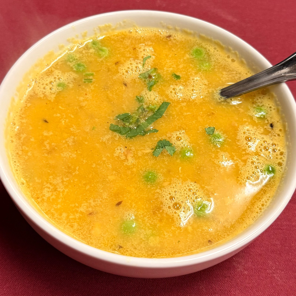 Bowl of golden, frothy soup garnished with chopped cilantro and green chilies, with a spoon resting inside.