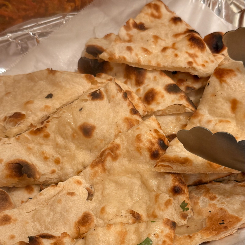 Stacked pieces of golden, blistered flatbread served in a foil-lined tray with serving tongs.