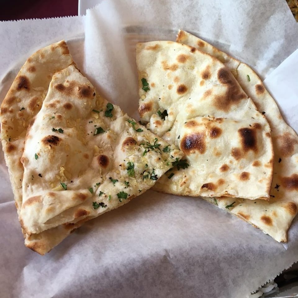 Golden-brown naan bread, some with garlic and herbs, served in a white paper-lined basket.