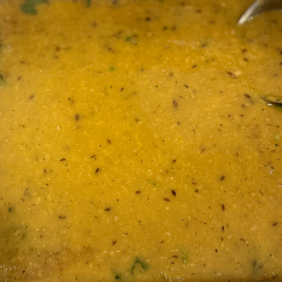 Close-up of creamy golden soup or curry seasoned with herbs and spices, with a spoon partially visible.