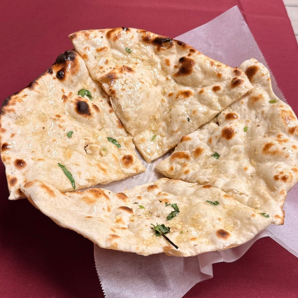 Stack of grilled naan bread pieces garnished with cilantro on a paper-lined plate over a red tablecloth.