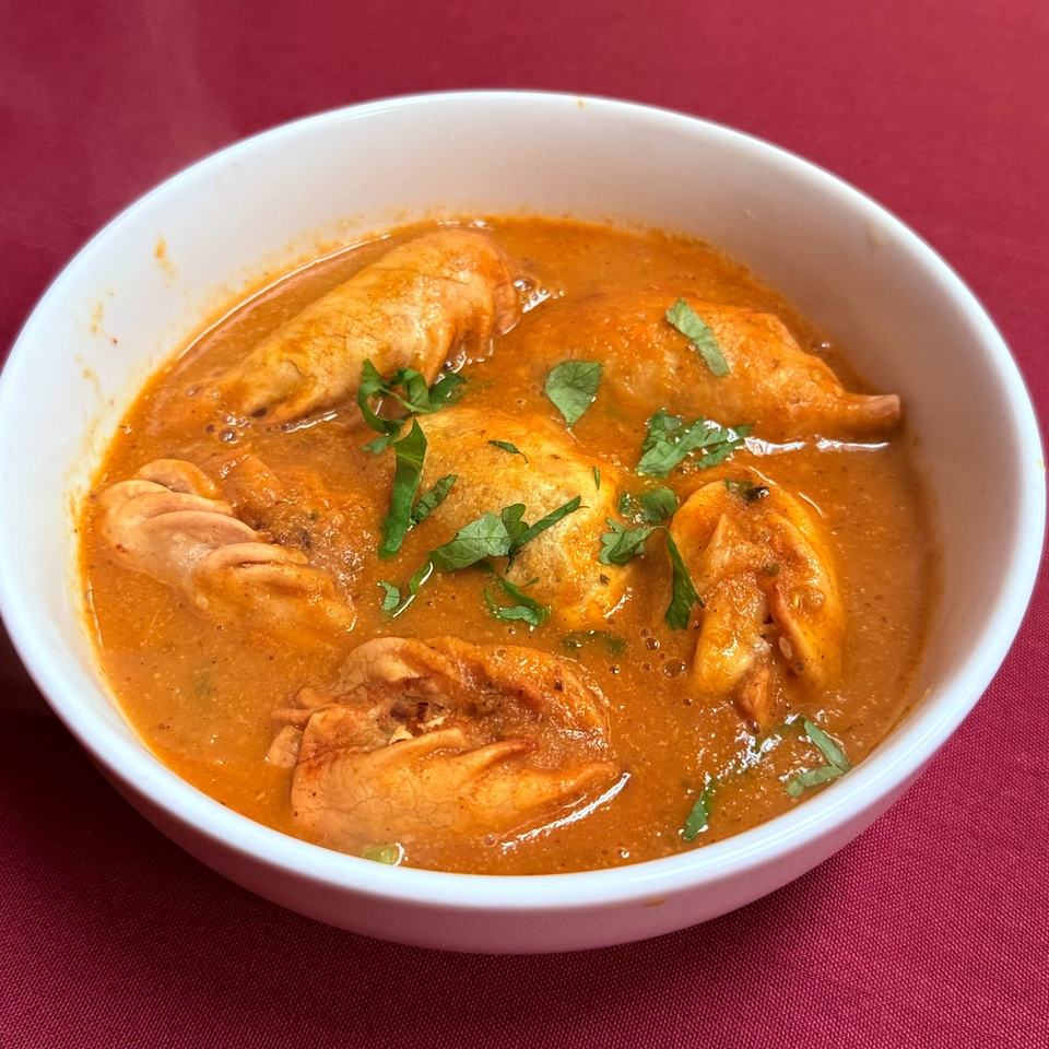 Bowl of orange curry containing several dumplings, garnished with fresh cilantro, on a red tablecloth.