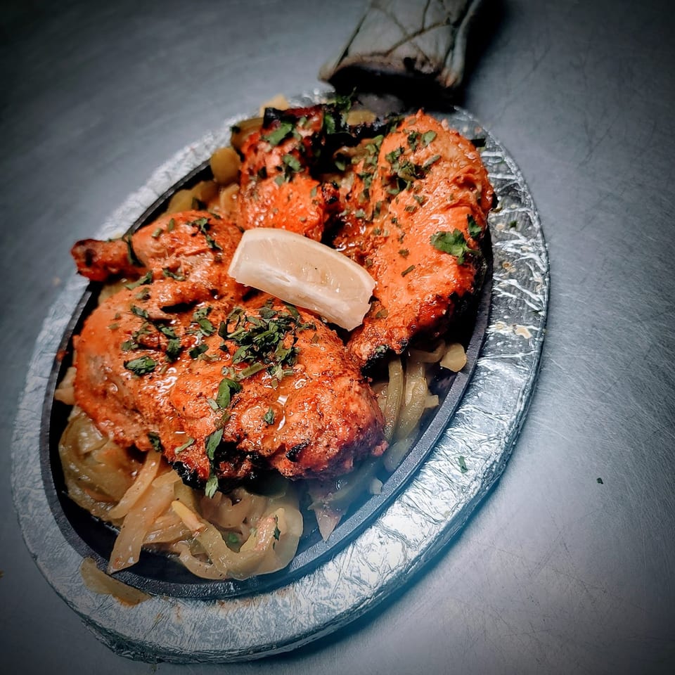 Sizzling Tandoori Chicken, garnished with cilantro and a lemon wedge, served on a bed of onions.