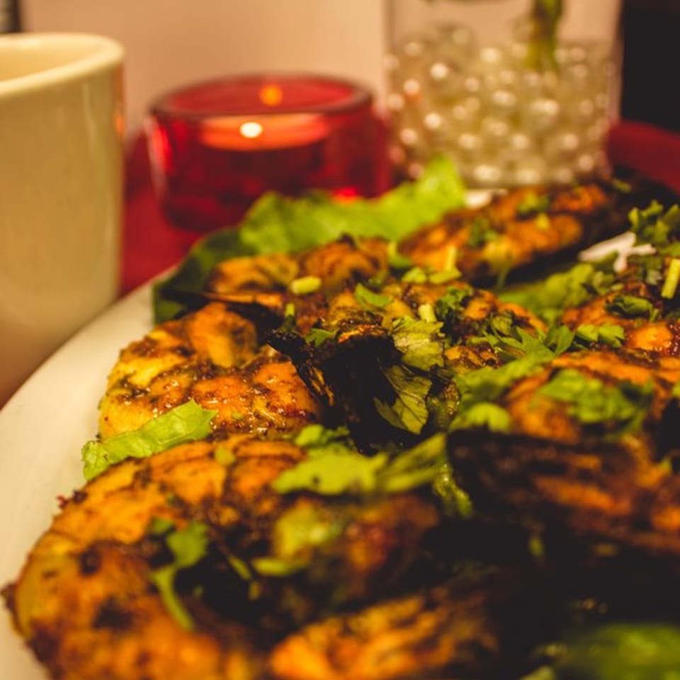 Close-up of Indian fish fry garnished with cilantro and lettuce, with a candle in the background.