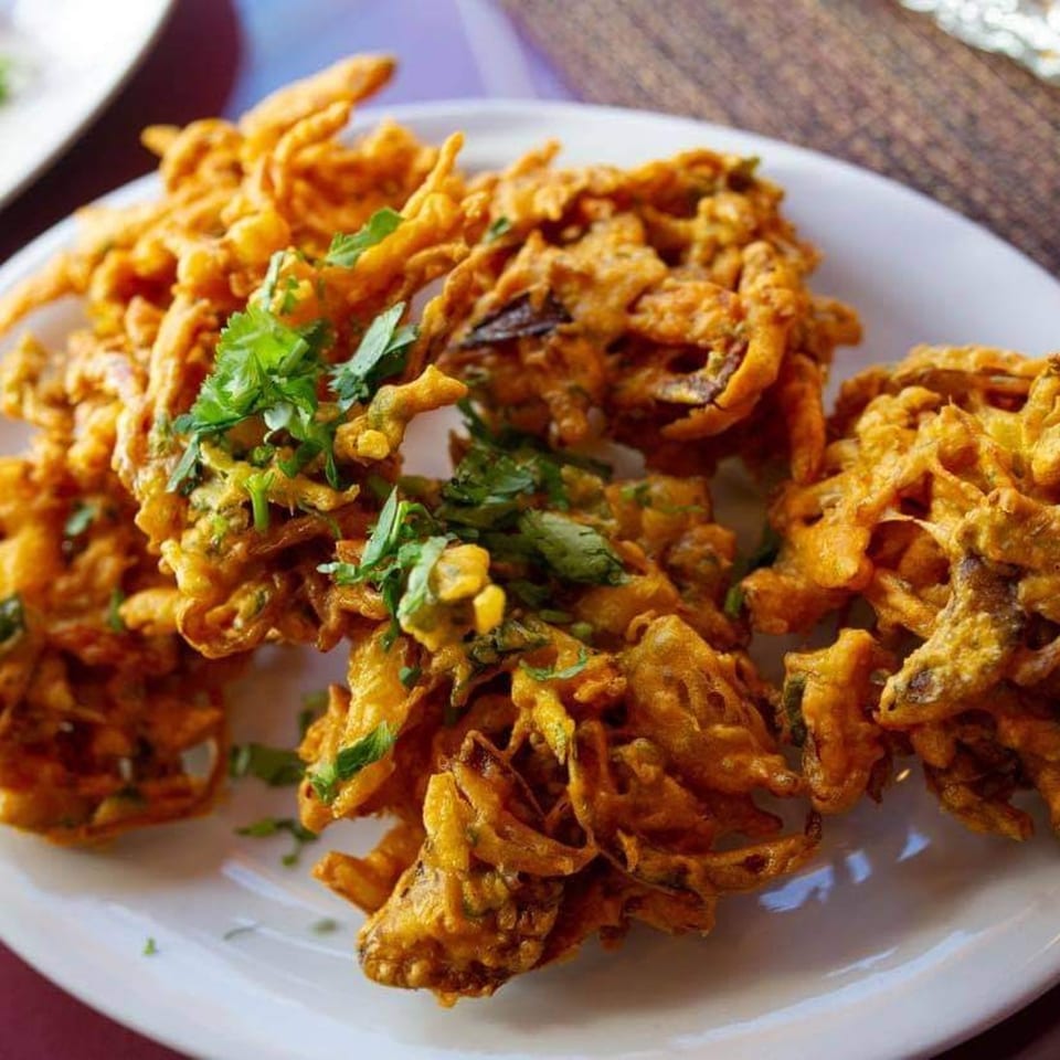 Crispy golden-brown Indian pakora, garnished with fresh green cilantro, served on a white plate.