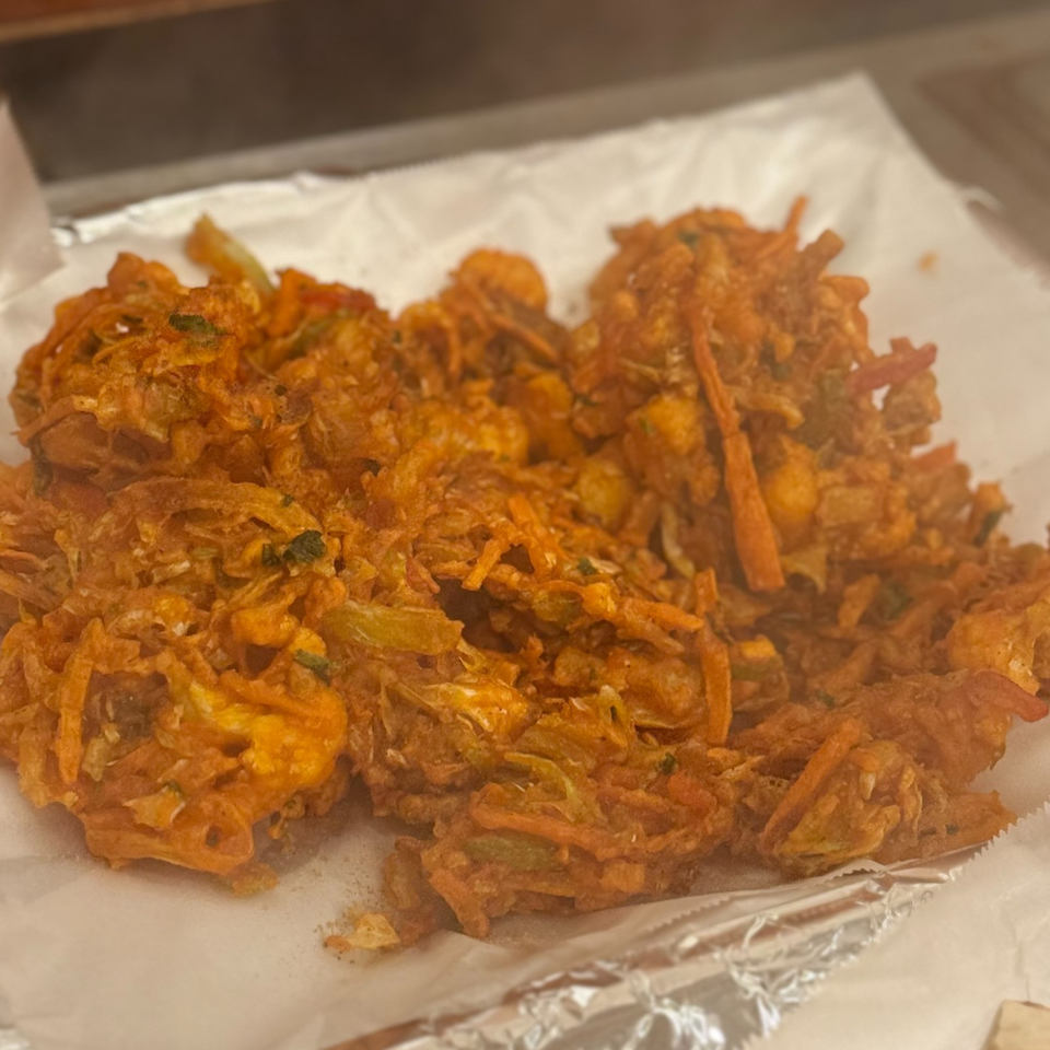 Crispy golden vegetable fritters piled on white paper over a foil-lined tray.
