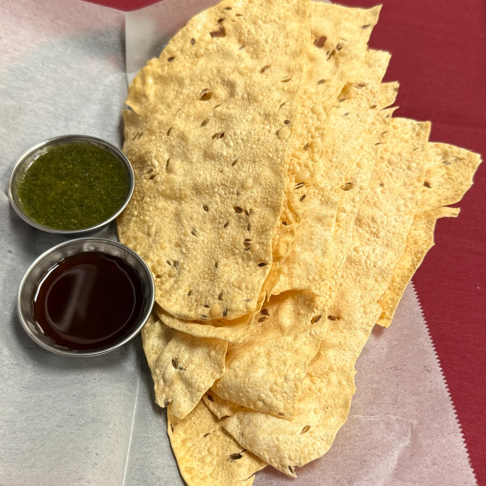 Stack of crisp, seed-speckled flatbreads served with green chutney and dark tamarind sauce.