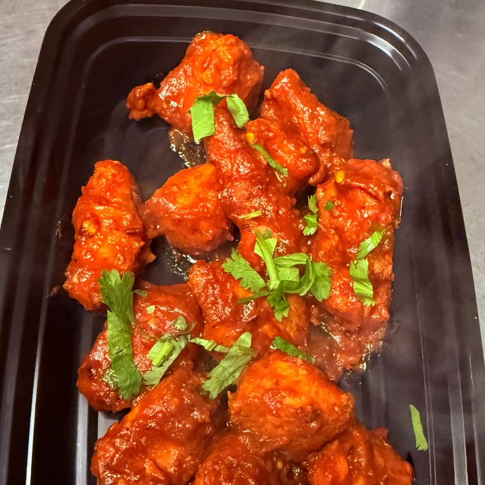 Spicy red-sauced chicken pieces garnished with fresh cilantro on a black rectangular serving tray.
