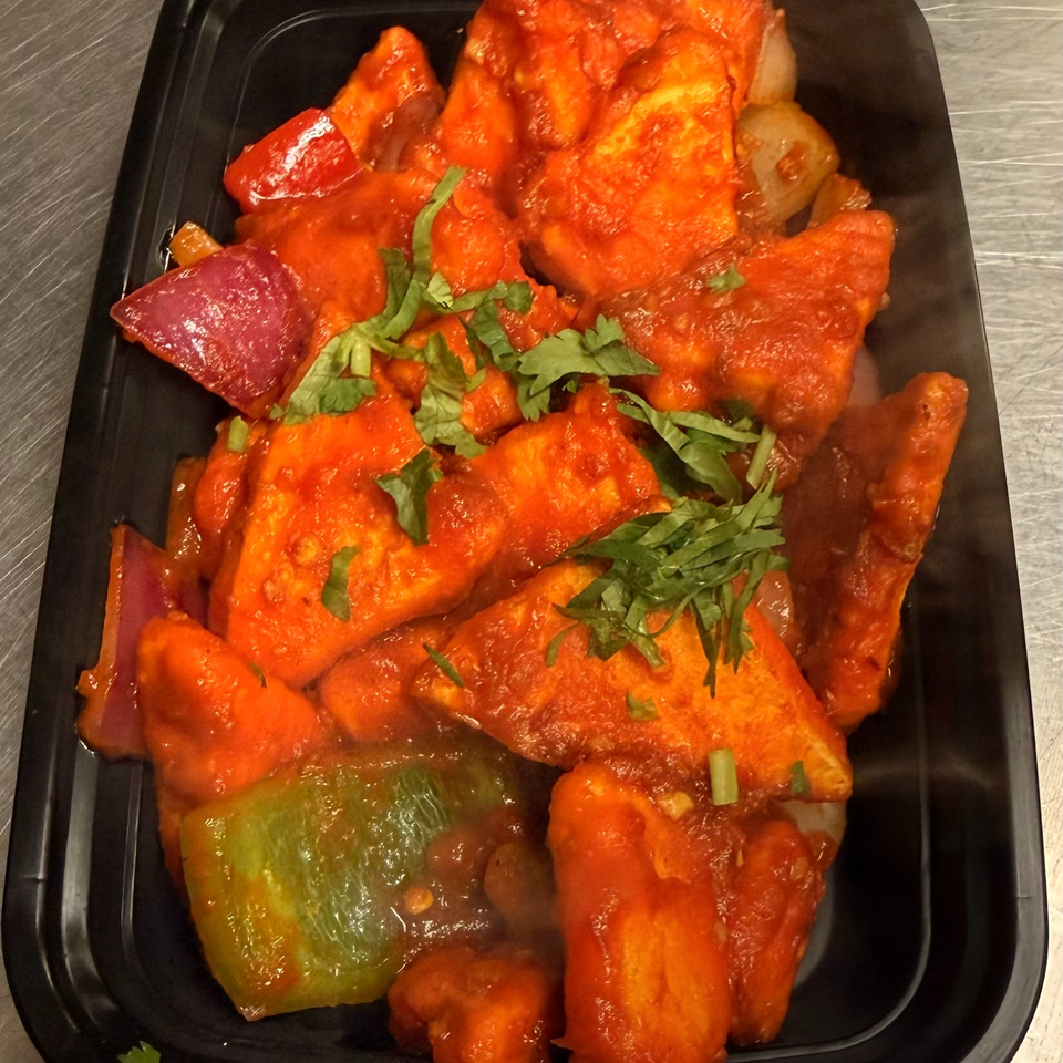 Vibrant orange-sauced paneer pieces with red and green peppers, onions, and cilantro in a black rectangular dish.