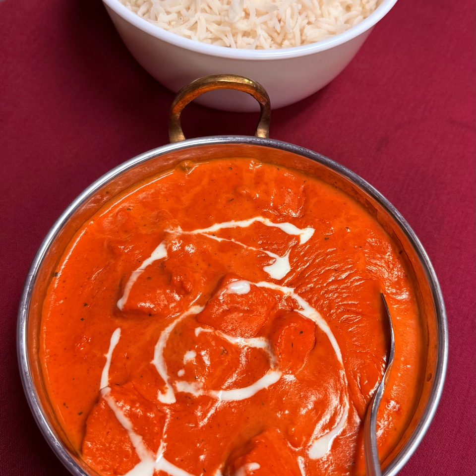 Creamy orange curry garnished with cream in a metal serving dish, accompanied by a bowl of white rice.
